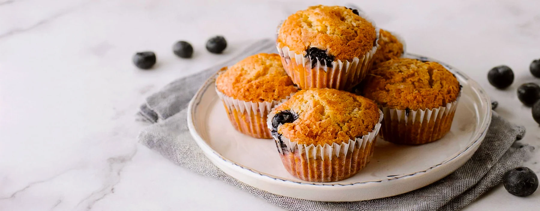 Golden blueberry muffins with fresh blueberries on a ceramic plate