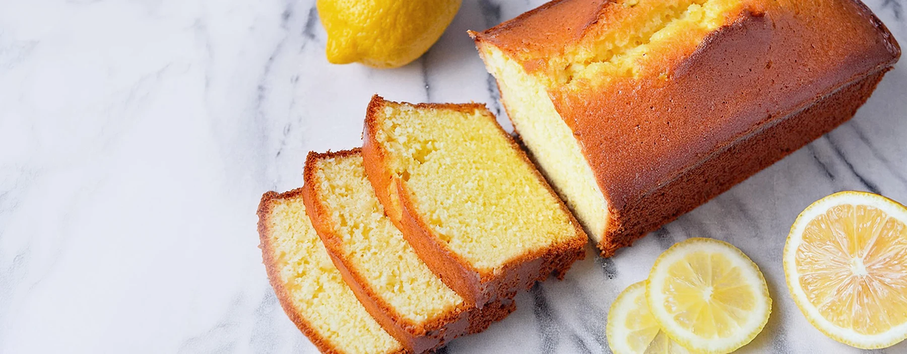 Freshly sliced golden lemon loaf and lemons on a marble surface